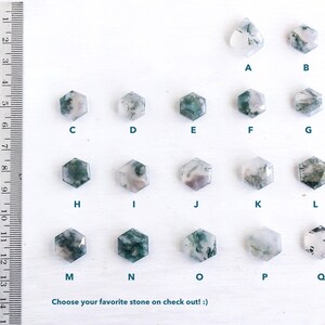 May include: A collection of seventeen moss agate stones in hexagonal and teardrop shapes, labeled A through Q, arranged in rows. A metal ruler on the left shows measurements in inches and centimeters. The text reads: Choose your favorite stone on check out! :)