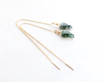 May include: A pair of gold-tone chain threader earrings featuring raw, faceted moss agate stones in shades of deep green and translucent white. Each stone is secured to the delicate metal chain with a small gold-colored wire wrap.