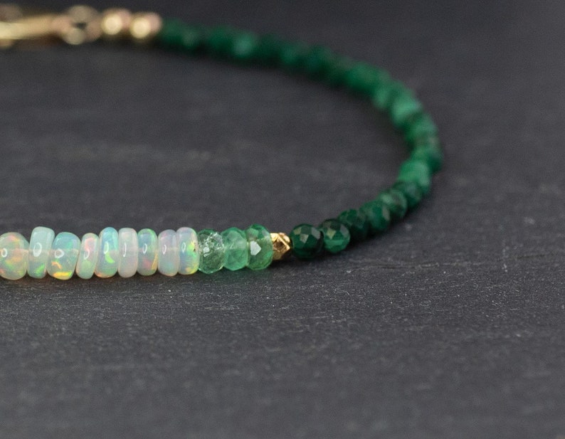 Puede incluir: Una delicada pulsera de cuentas que presenta una secuencia de rondeles de &oacute;palo blanco iridiscente, seguidos de peque&ntilde;as cuentas de esmeralda verde facetadas y una cuenta espaciadora dorada, terminada con un cierre dorado en el extremo.