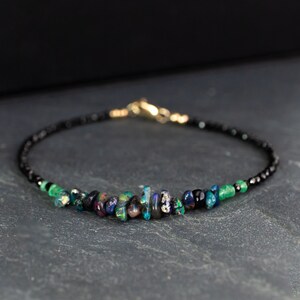Puede incluir: Una pulsera delicada que presenta una hilera de peque&ntilde;as cuentas negras facetadas, acentuada con una fila central de fragmentos de &oacute;palo iridiscente en bruto y peque&ntilde;as cuentas de piedras preciosas verdes, con cierre de mosquet&oacute;n dorado.