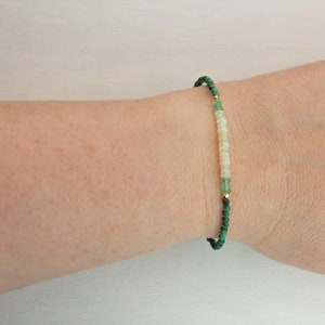 Puede incluir: Una pulsera delicada con peque&ntilde;as cuentas redondas de color verde oscuro, intercaladas con una secci&oacute;n central de cuentas blancas p&aacute;lidas e iridiscentes. El dise&ntilde;o incluye diminutas cuentas espaciadoras de metal dorado que separan los segmentos.