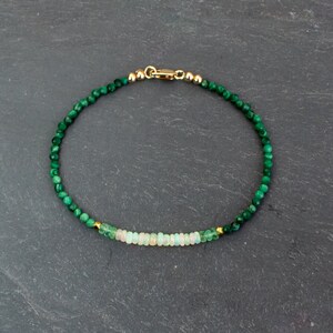 Puede incluir: Una delicada pulsera de cuentas con peque&ntilde;as cuentas facetadas de malaquita verde oscuro y una fila central de cuentas rondelle p&aacute;lidas e iridiscentes similares al &oacute;palo. La pulsera tiene un cierre de mosquet&oacute;n dorado y peque&ntilde;as cuentas espaciadoras doradas.