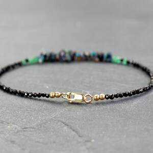 Puede incluir: Una pulsera delicada que presenta una hilera de peque&ntilde;as cuentas negras facetadas, acentuada con un grupo central de fragmentos de piedra azul oscuro y verde. La pieza se completa con un cierre de mosquet&oacute;n dorado y peque&ntilde;as cuentas espaciadoras doradas.