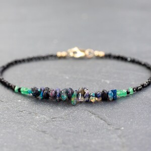Puede incluir: Una pulsera delicada que presenta una hilera de peque&ntilde;as cuentas negras, acentuada con una fila central de fragmentos de &oacute;palo iridiscente y peque&ntilde;as cuentas de piedras preciosas verdes. La pieza incluye un cierre de mosquet&oacute;n de metal dorado.