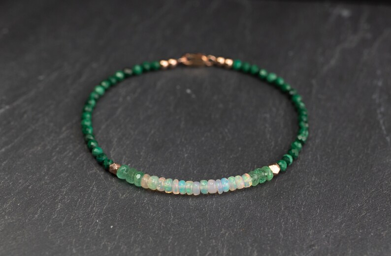 Puede incluir: Una pulsera de cuentas con una hilera de peque&ntilde;as cuentas de malaquita verde oscuro facetadas, acentuada con una fila central de rondeles de &oacute;palo blanco iridiscente y peque&ntilde;as cuentas espaciadoras met&aacute;licas en tono oro rosa, con un cierre met&aacute;lico a juego.
