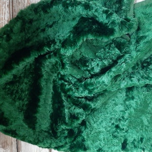 May include: A close-up of a deep green faux fur fabric. The fabric has a soft, plush texture and is perfect for crafting projects.