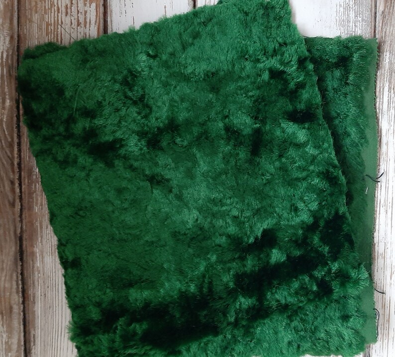 May include: Two pieces of dark green faux fur fabric. The fabric has a soft, plush texture.