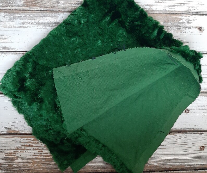 May include: A green velvet fabric with a fuzzy texture and a plain green fabric backing. The two fabrics are sewn together along the edges.