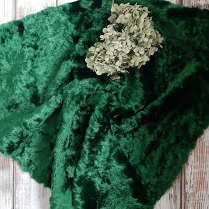 May include: A deep green faux fur fabric with a soft, plush texture. The fabric is folded and draped, creating a luxurious and inviting look.