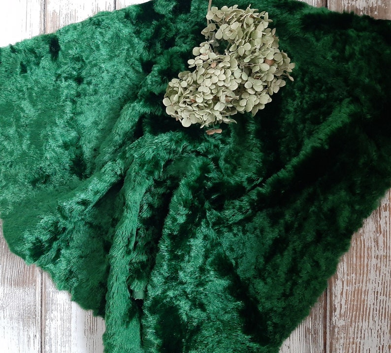 May include: A deep green faux fur fabric with a soft, plush texture. The fabric is folded and draped, creating a luxurious and inviting look.