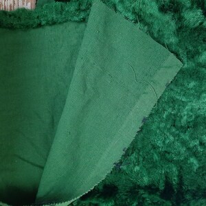 May include: A close-up of a dark green fabric with a fuzzy texture. The fabric is folded in half, revealing a smooth, dark green underside.