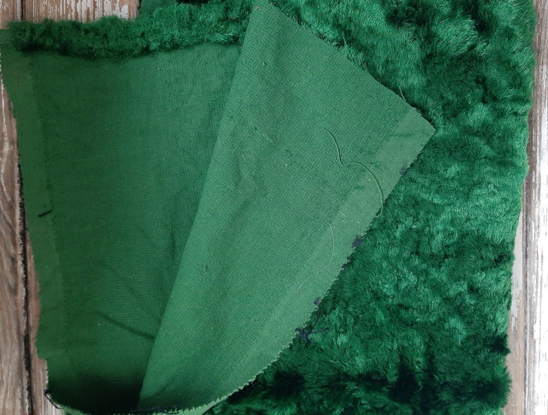 May include: A close-up of a dark green fabric with a fuzzy texture. The fabric is folded in half, revealing a smooth, dark green underside.