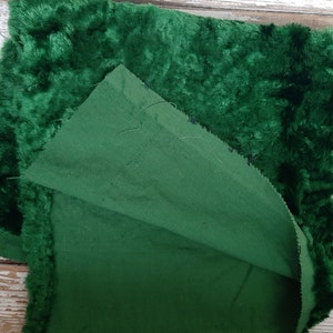 May include: A close-up of two pieces of fabric, one a dark green velvet and the other a dark green cotton. The velvet is folded over the cotton, showing the back side of the velvet.