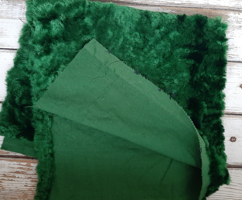 May include: A close-up of two pieces of fabric, one a dark green velvet and the other a dark green cotton. The velvet is folded over the cotton, showing the back side of the velvet.