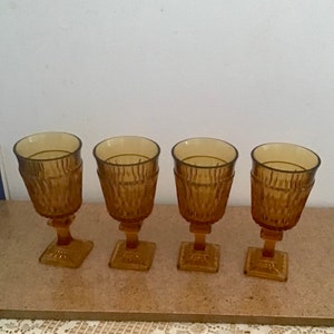 May include: Set of four amber glass goblets with a textured design. The goblets have a square base and a round bowl.