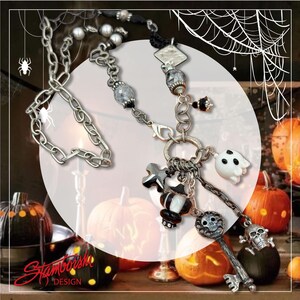 May include: A silver-toned Halloween-themed necklace with various charms, including a ghost, key, skull, and cross. The necklace features a chain design with decorative beads and a lobster clasp. The background includes pumpkins, a spider web, and a spider.