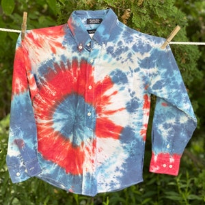 May include: A long-sleeved button-down shirt with a tie-dye pattern in shades of red, blue, and white. The shirt has a single pocket on the left chest.