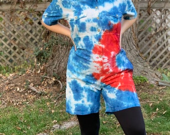 May include: A person wearing a blue and red tie-dye jumpsuit with black leggings and a blue and white baseball cap. They are wearing a red patterned face mask.