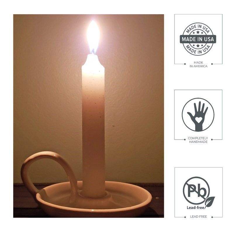 May include: A white candle with a flame burning in a white ceramic candle holder with a handle. The candle is made in the USA, is completely handmade, and is lead-free.