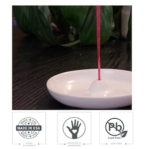 May include: White ceramic incense holder with a small, raised center for holding incense sticks. A red incense stick is burning in the holder. The holder is made in the USA and is lead-free.