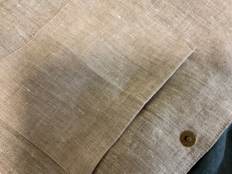 May include: Close-up of a beige linen fabric with a large pocket and a small metal button.
