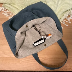 May include: A blue linen tote bag with a light brown linen lining. The bag is open and has a cell phone and glasses inside.