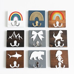 Pode incluir: Nove ganchos de parede de madeira com diferentes designs, incluindo arco-&iacute;ris, montanhas, um la&ccedil;o, um dinossauro, um tubar&atilde;o, um urso e uma sereia. Cada gancho tem dois ganchos prateados.