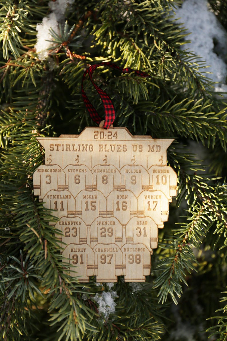 May include: A wooden hockey ornament with the text "Stirling Blues U9 MD" and the game time "20:24". The ornament features a team roster with player names and jersey numbers.