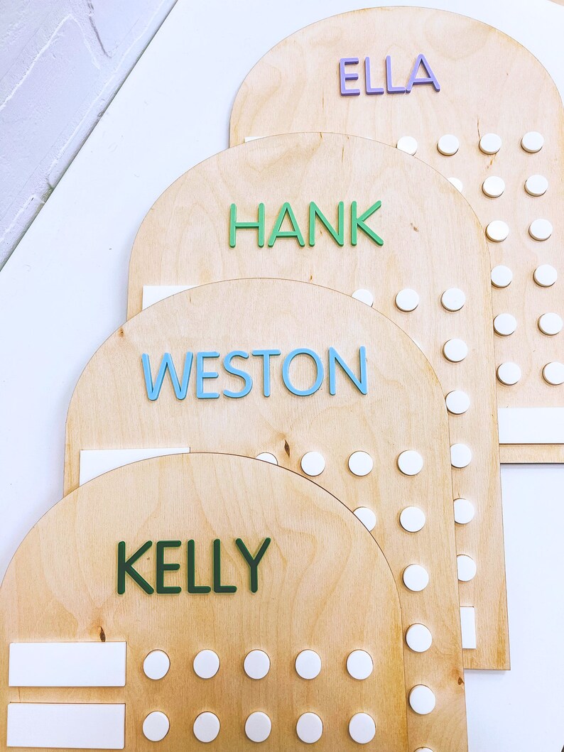 May include: Four wooden arch-shaped boards with white circles and names written in colorful letters. The names are Ella, Hank, Weston, and Kelly.