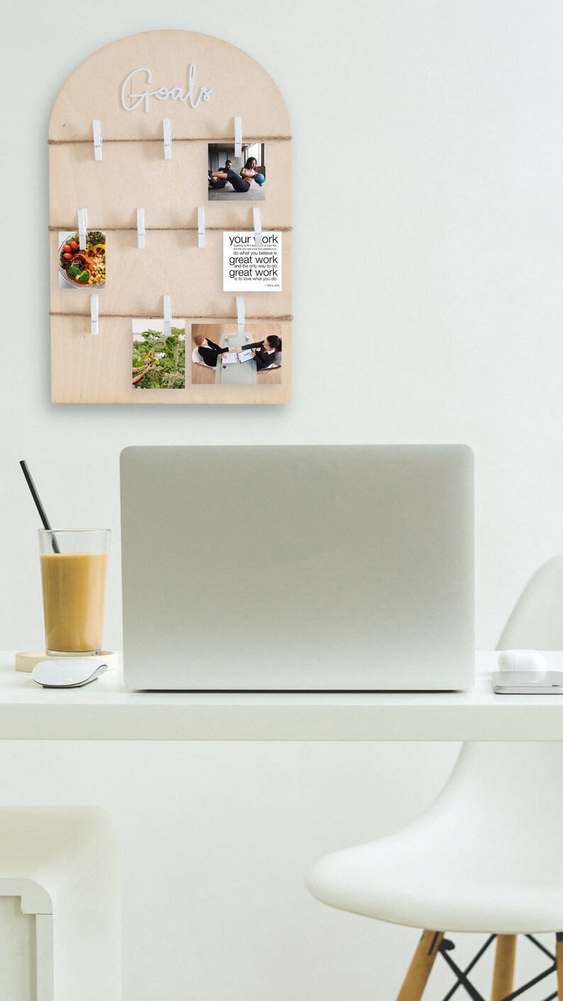 May include: A wooden board with the word "Goals" written in white letters. The board has multiple clothespins holding photos and a card with the text "Your work is your work do what you believe in great work comes from great work love what you do".