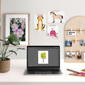 May include: A vision board with a wooden frame and string, with various photos and cards clipped to it. The board has the text "Vision Board" written on it. The board is on a white desk with a laptop, a potted plant, and other items.