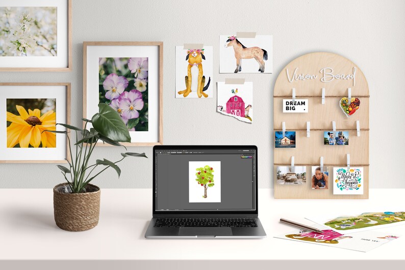 May include: A vision board with a wooden frame and string, with various photos and cards clipped to it. The board has the text "Vision Board" written on it. The board is on a white desk with a laptop, a potted plant, and other items.