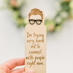 May include: Wooden bookmark featuring a cartoon illustration of a person wearing glasses and the text "I'm trying very hard not to connect with people right now."