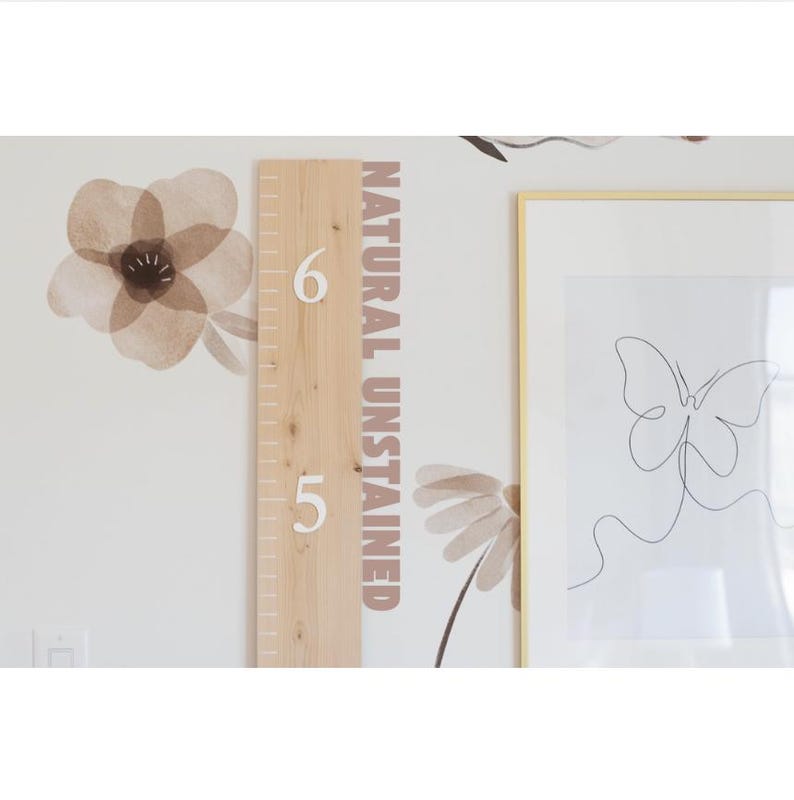 May include: A wooden growth chart with white numbers, a natural unstained finish, and a white background with brown floral decals. The chart is mounted on a wall with a framed picture of a butterfly.