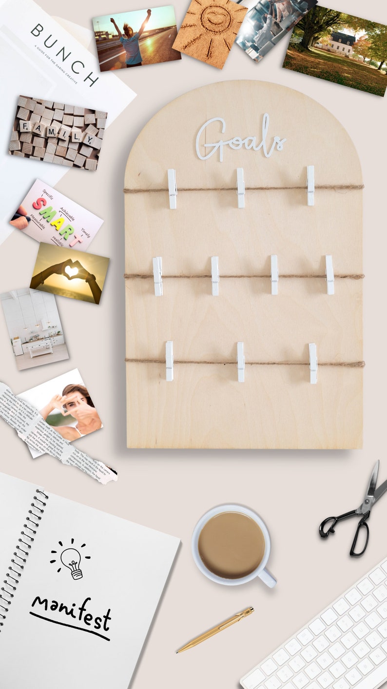 May include: A wooden board with the word "Goals" written in white lettering. The board has a rounded top and is decorated with twine and white clothes pegs. There are several photos and cards pinned to the board, including a photo of a heart made with hands, a photo of a family, and a card with the word "SMART" written on it.
