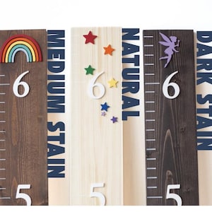 May include: Four wooden growth charts with different stain colors: natural, medium stain, dark stain. Each chart features a number 6 and a design: a rainbow, stars, and a fairy.
