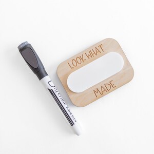 May include: A wooden sign with the text "LOOK WHAT I MADE" and a blank oval space in the center. A dry erase marker is next to the sign.