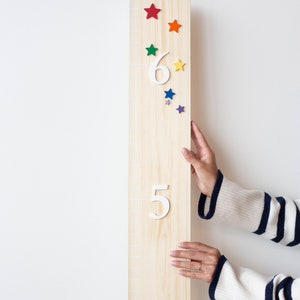 Puede incluir: Un gr&aacute;fico de crecimiento de madera con los n&uacute;meros blancos 4, 5 y 6. El gr&aacute;fico est&aacute; decorado con estrellas de colores. Una mano est&aacute; llegando hacia el gr&aacute;fico.