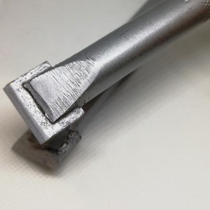 Puede incluir: Una herramienta de metal plateado con un mango rectangular y una punta puntiaguda. La herramienta está diseñada para manualidades y creación.