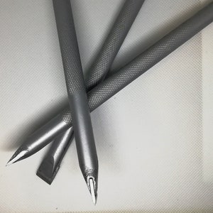 Puede incluir: Tres herramientas de metal plateado con puntas puntiagudas y mangos texturados. Las herramientas están dispuestas en forma de V sobre una superficie blanca.