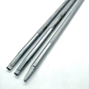 Puede incluir: Tres herramientas de metal plateado con puntas de diferentes formas. Las herramientas tienen un mango texturizado.