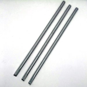 Puede incluir: Tres herramientas de metal plateado con una superficie texturizada y una punta plana ligeramente redondeada. Las herramientas están dispuestas en fila, con la herramienta más larga en la parte superior y la más corta en la parte inferior.