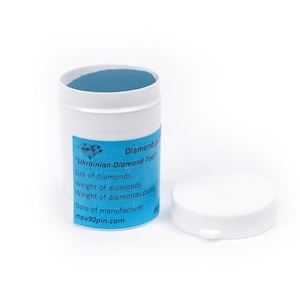 Op de afbeelding: Een witte cilindrische container met een blauw interieur en een los deksel. Een blauw label op de container leest "Ukrainian Diamond Tool" en bevat tekst over diamantgrootte en -gewicht. De website mpx90pin.com is ook zichtbaar.