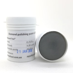 Könnte beinhalten: Zwei weiße Kunststoffbehälter mit Diamant-Polierpaste. Ein Behälter ist geschlossen, der andere ist offen und zeigt eine graue Paste. Das Etikett lautet "Diamond polishing paste 0,25" und "Diamond Tool". Die Paste hat 4,00 Karat.