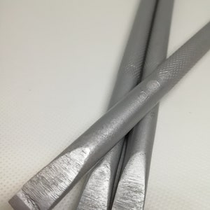 Op de afbeelding: Drie zilveren metalen beitels met afgeronde uiteinden. De beitels zijn op elkaar gestapeld.
