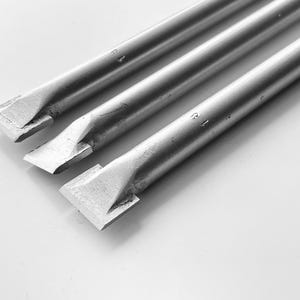Może przedstawiać: Trzy srebrne metalowe dłuta z płaskimi, fazowanymi krawędziami ułożone są po przekątnej na białym tle. Dłuta mają cylindryczne trzony i są oznaczone numerem "13".