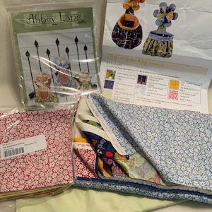 May include: A quilting kit for making a small bag with a floral pattern. The kit includes fabric, instructions, and a pattern for the "Abbey Bag" project.