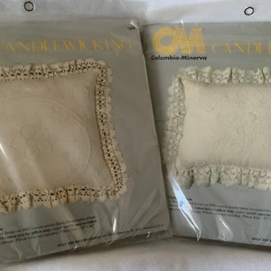 May include: Two white pillow kits with lace trim and floral embroidery. The kits are packaged in plastic and labeled "Candlewicking" with the brand name "Columbia-Minerva".