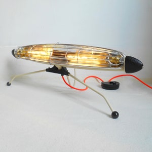 Puede incluir: Una lámpara moderna de mediados de siglo, blanca y cromada, con una pantalla en forma de jaula y un cable rojo. La lámpara tiene una base negra y tres patas.