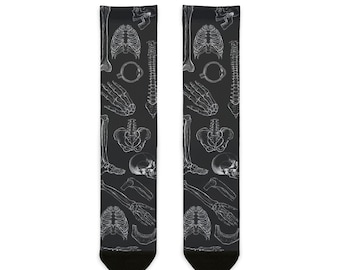 May include: A pair of black socks with a white anatomical skeletal pattern. The pattern includes bones, skulls, and ribs.